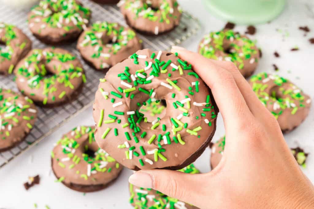 Hand holding a homemade Chocolate Mint Donut topped with mint chocolate and green sprinkles