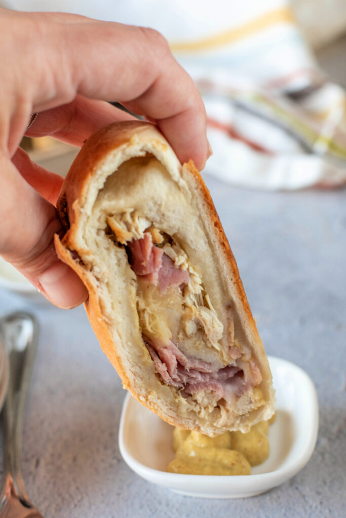 hand dipping chicken cordon bleu stromboli slice into mustard