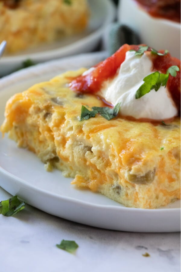 closeup of chilies rellnos bake slice garnished with sour cream and salsa on plate