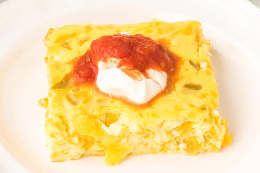 Slice of Chilies Rellenos Bake topped with sour cream and salsa on a white plate