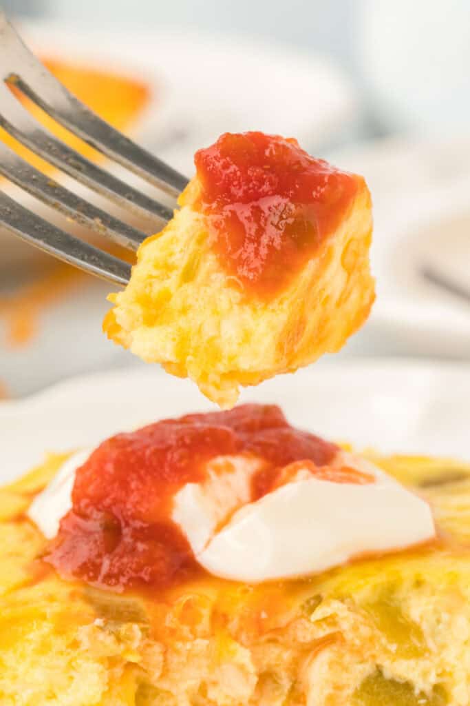 Fork holding a bite of Chilies Rellenos Bake topped with salsa above the casserole