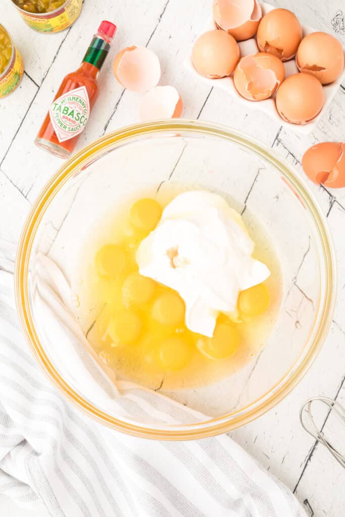 Eggs, sour cream, salt, and hot sauce in a glass mixing bowl for Chilies Rellenos Bake