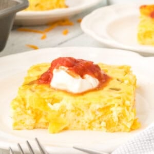 Square image of Chilies Rellenos Bake topped with sour cream and salsa on a white plate