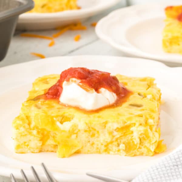 Square image of Chilies Rellenos Bake topped with sour cream and salsa on a white plate