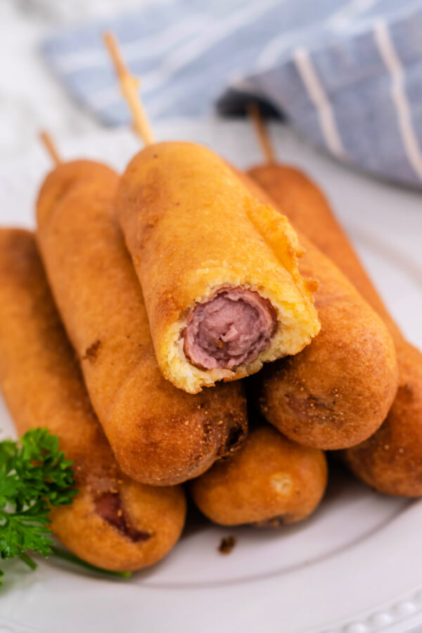 corn dogs stacked on plate with a bite taken out of the top one