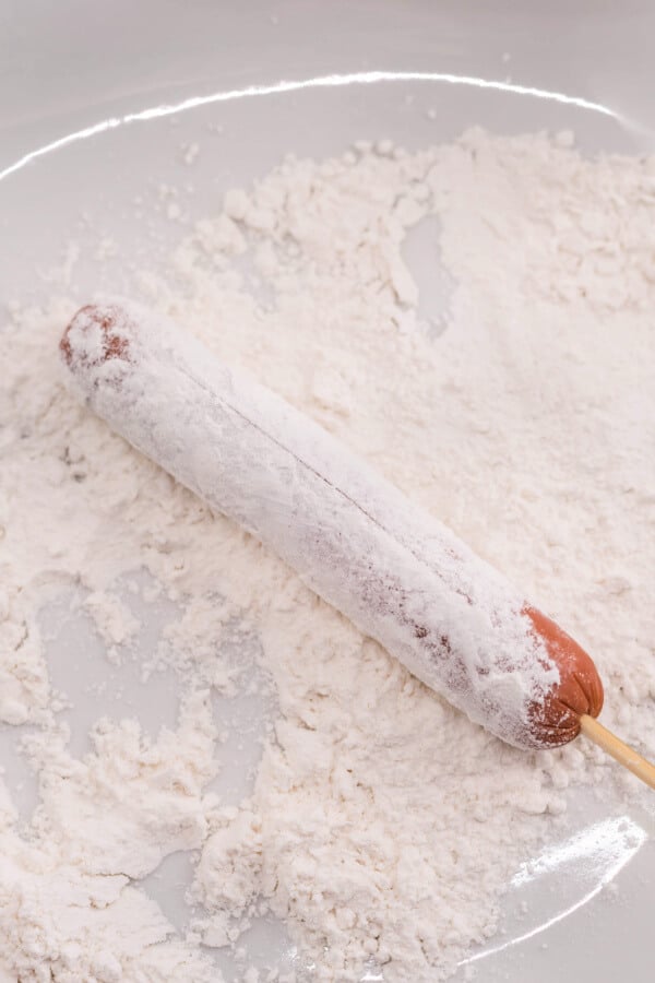 coating the skewered hot dog in flour
