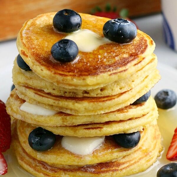 Closeup of a stack of pancakes with blueberries and maple syrup.