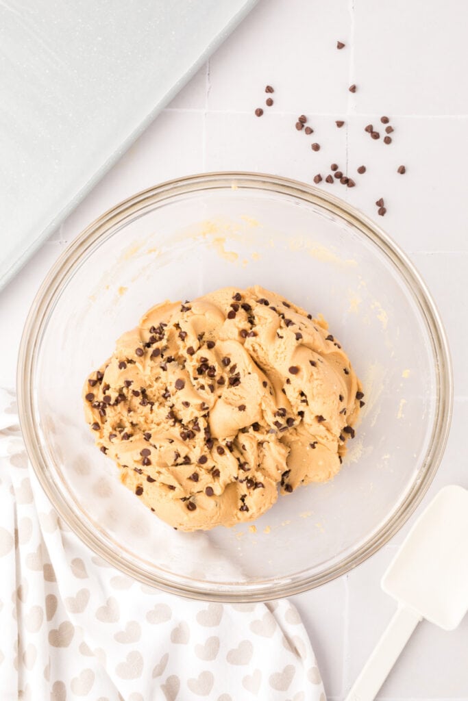Cookie dough fully mixed with chocolate chips in a large glass mixing bowl.
