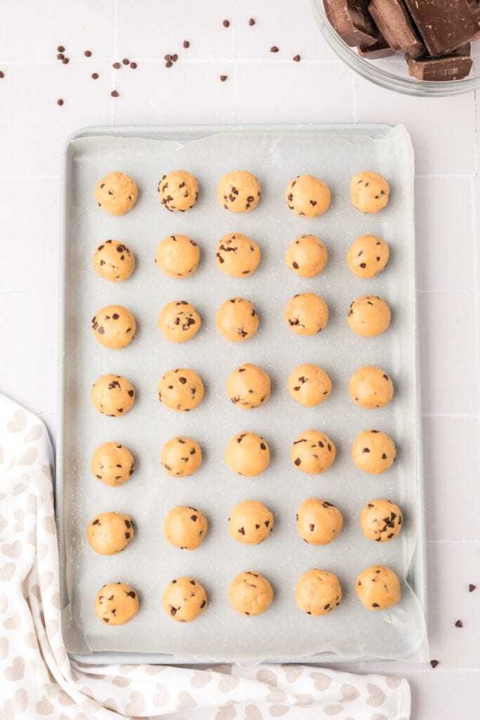 Rolled chocolate chip cookie dough balls arranged neatly on a wax paper lined baking sheet before dipping in chocolate.