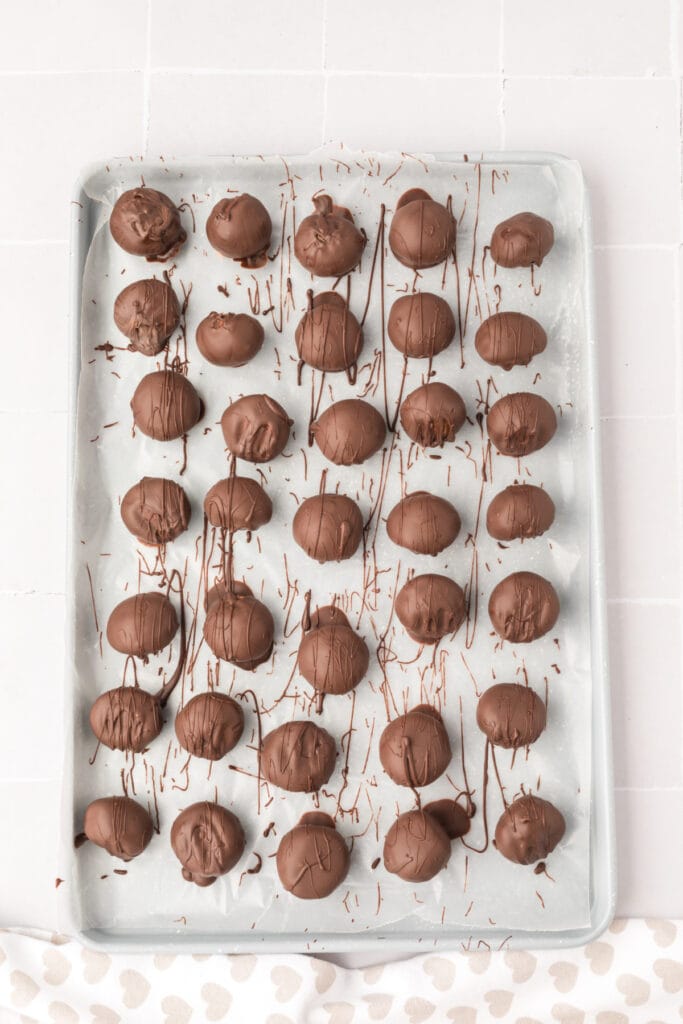 Baking sheet filled with freshly dipped chocolate-covered cookie dough truffles, drizzled with extra chocolate.