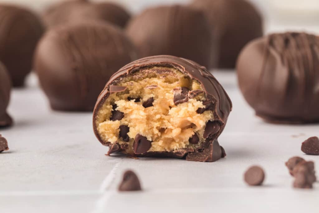 Close-up of bitten truffle on a white surface with more truffles blurred in the background.