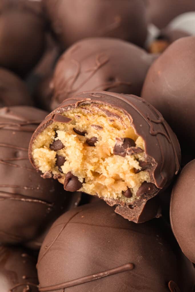 Pile of chocolate chip cookie dough truffles with one cut open to reveal soft cookie dough filling.