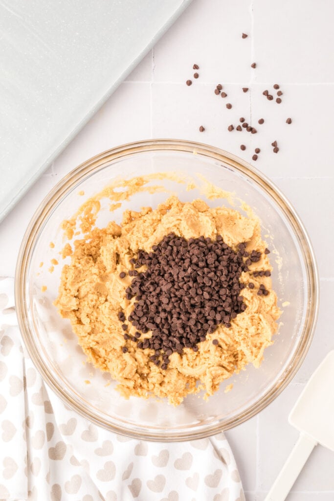 Mini chocolate chips added to the cookie dough mixture in a glass bowl.