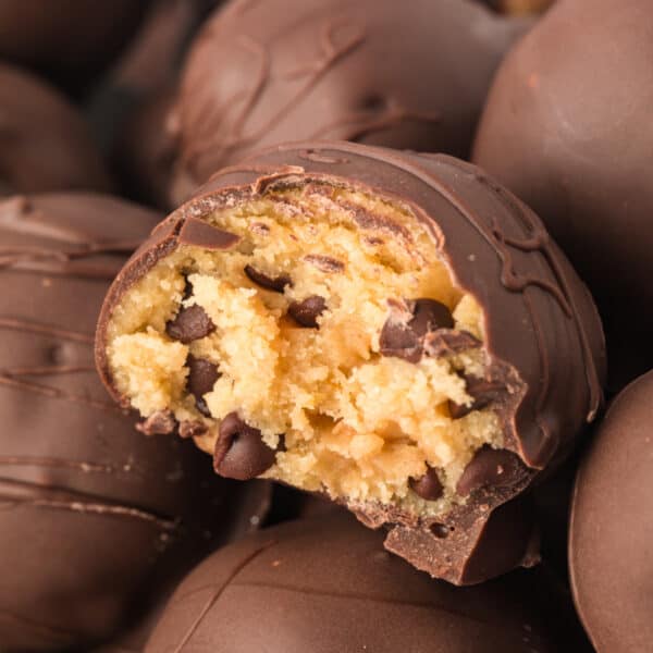 Square close-up of a bitten chocolate truffle with cookie dough filling and mini chocolate chips inside.