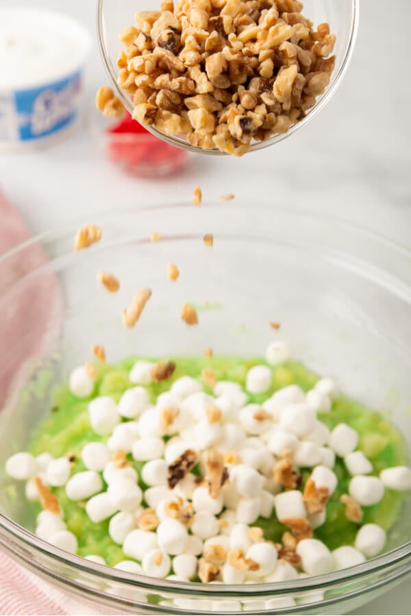 marshmallows and nuts being added to the pineapple-pudding mixture