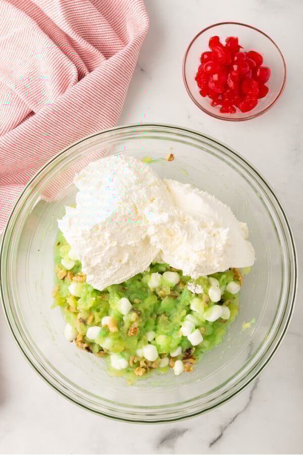 whipped topping added to bowl with a bowl of cherries off to the side