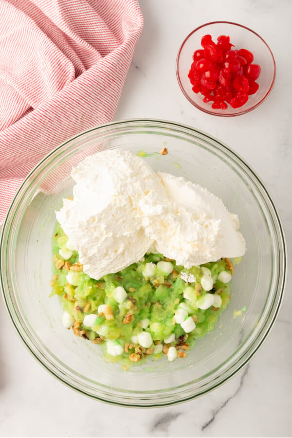 whipped topping added to bowl with a bowl of cherries off to the side