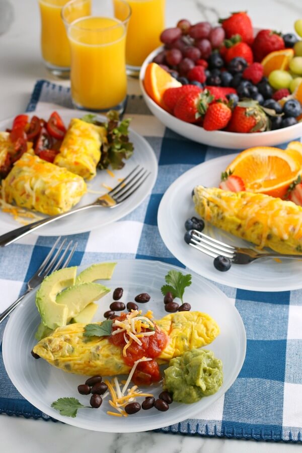 table spread with plates with omelets, orange juice , and a bowl of berries