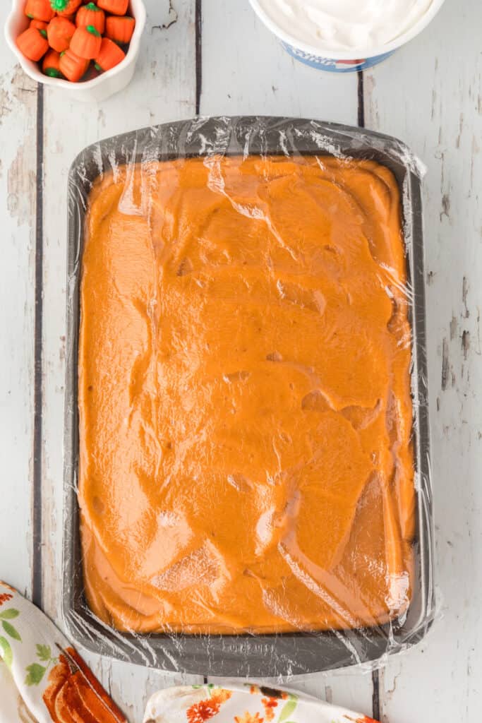 Plastic wrap covering the chilled pumpkin pudding cake in the pan