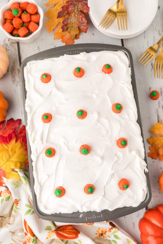 Pumpkin poke cake topped with candy pumpkins and surrounded by fall decor