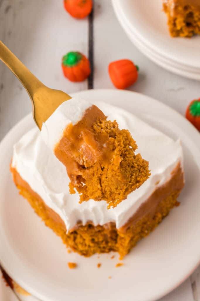 Fork holding a bite of pumpkin poke cake with pudding and whipped topping