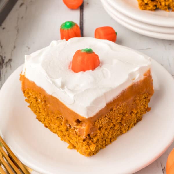 Square close-up of a slice of pumpkin poke cake with whipped topping