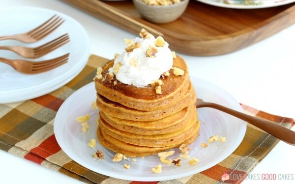 Pumpkin pancakes stacked up on a plate with a fork.