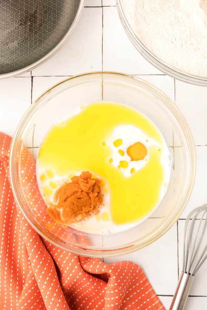 Wet ingredients including pumpkin purée, milk, oil, and egg in a glass bowl ready to be mixed