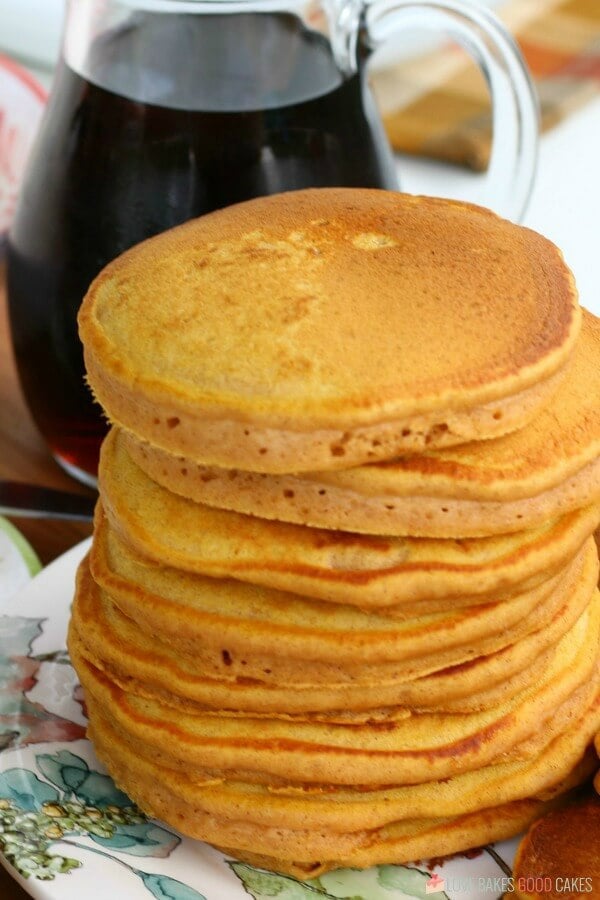 Pumpkin pancakes stacked up on a plate with a bottle of syrup