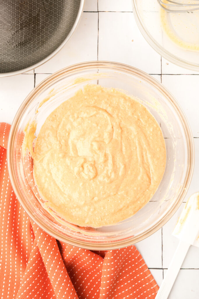 Smooth pumpkin pancake batter in a glass mixing bowl with spatula on the side