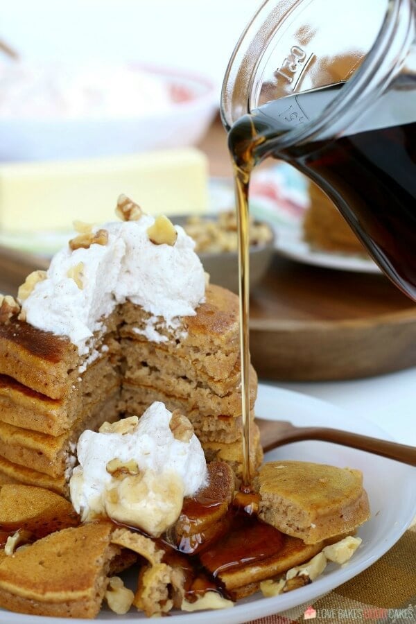 Pumpkin pancakes stacked up on a plate with syrup being poured over the top.