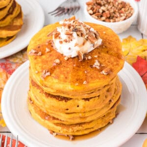 Square crop of pumpkin pancakes topped with whipped cream, chopped pecans, and syrup for a cozy fall breakfast scene