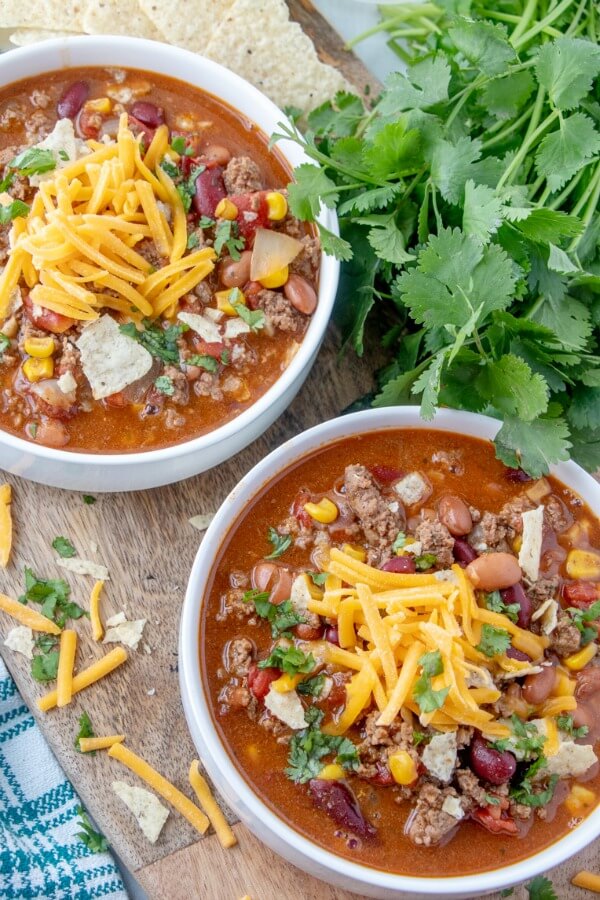 Taco Soup is a hearty and satisfying recipe with plenty of ground beef, beans, corn, and tomatoes in a zesty taco flavored broth. two bowls of Taco Soup with tortilla chips and cilantro