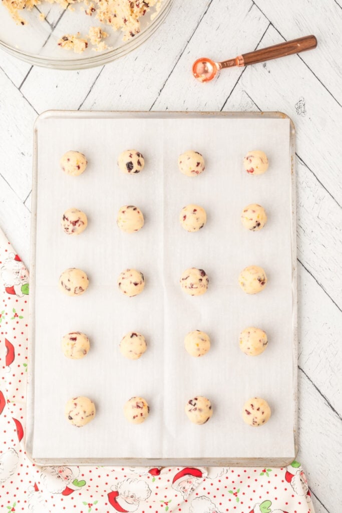 Dough balls of Cranberry Orange Christmas Sandies evenly spaced on a parchment-lined baking sheet, ready to bake.