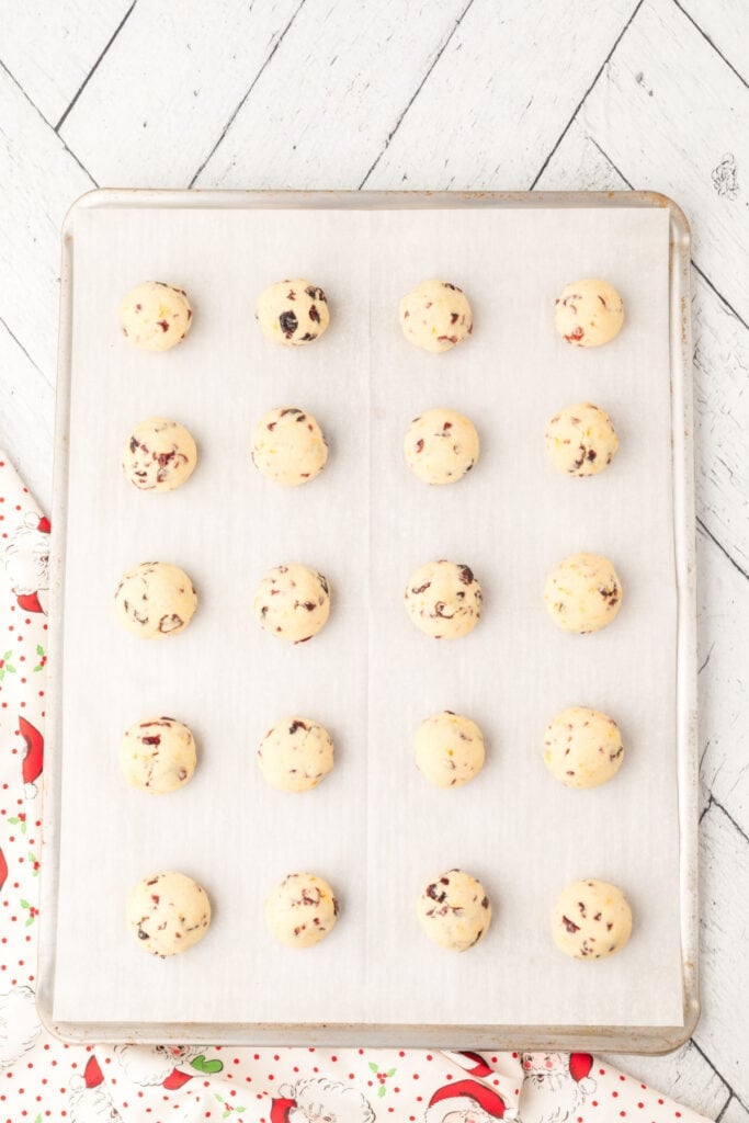 Baked Cranberry Orange Christmas Sandies cookie dough balls evenly spaced on a parchment-lined baking sheet, ready to bake.