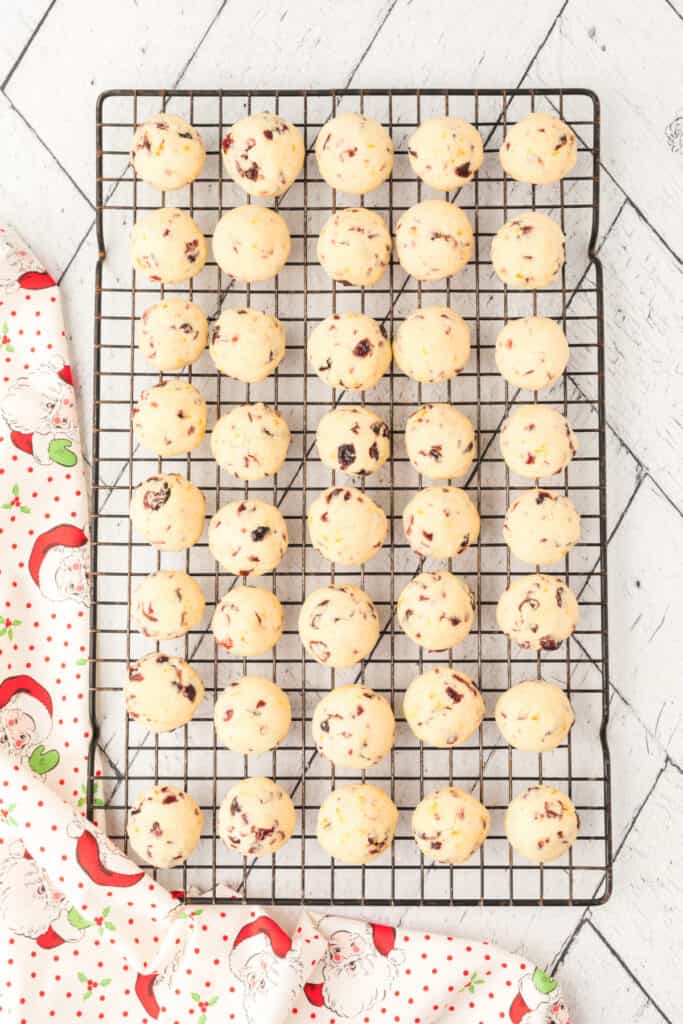 Freshly baked Cranberry Orange Christmas Sandies cooling on a wire rack with a festive Santa-patterned fabric underneath.