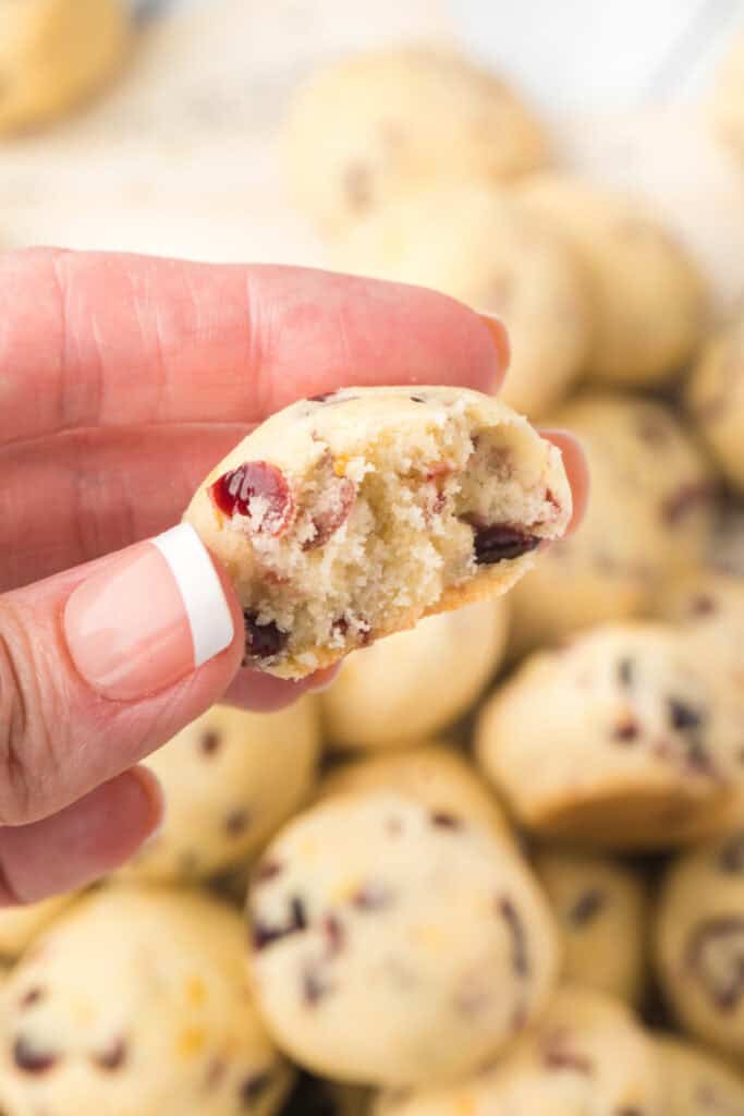 Hand holding a half-eaten Cranberry Orange Christmas Sandies cookie to reveal the soft, buttery interior with cranberries.
