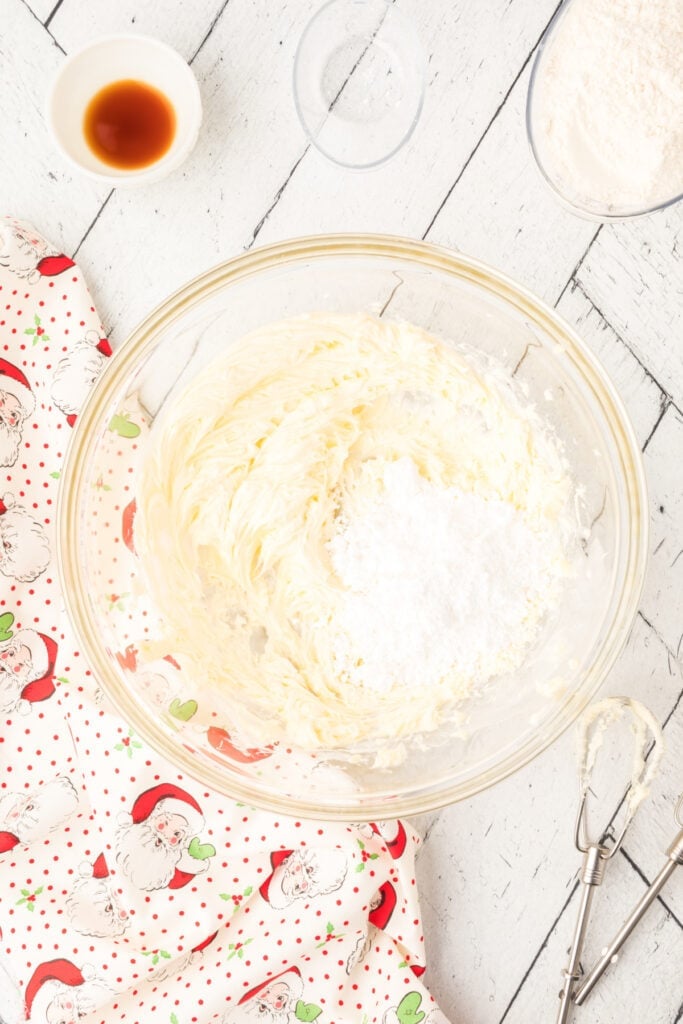 Butter mixture with powdered sugar being added to the bowl for Cranberry Orange Christmas Sandies dough preparation.