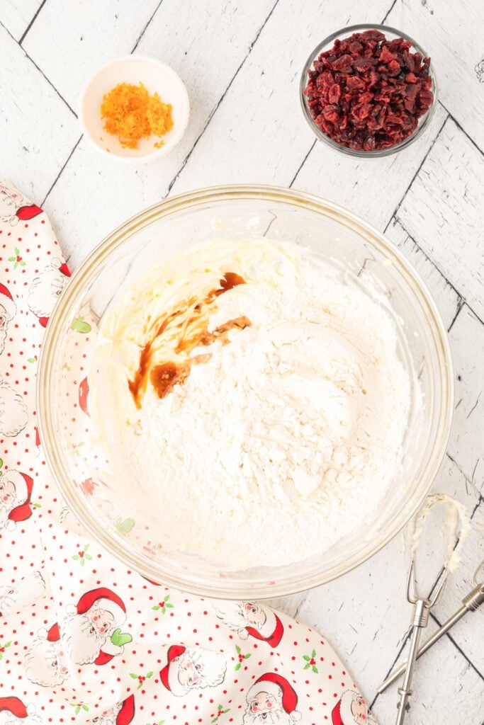 Flour and vanilla added to the butter mixture in the bowl, ready to be mixed into the Cranberry Orange Christmas Sandies dough.