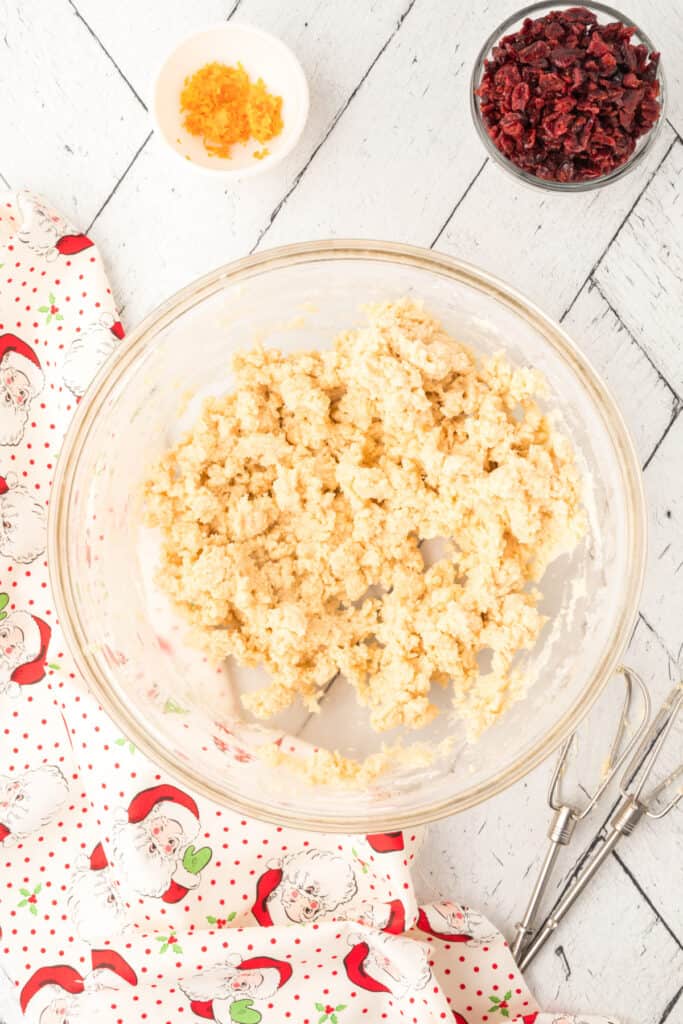 Partially mixed cookie dough showing crumbly texture before cranberries and orange zest are added.
