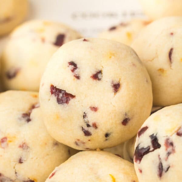 Close-up square crop of Cranberry Orange Christmas Sandies cookie with visible dried cranberries and orange zest on a light background.