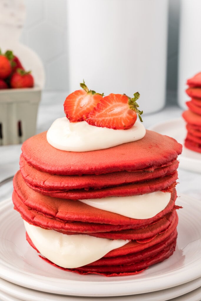 red velvet pancakes with cream cheese icing stacked on plate