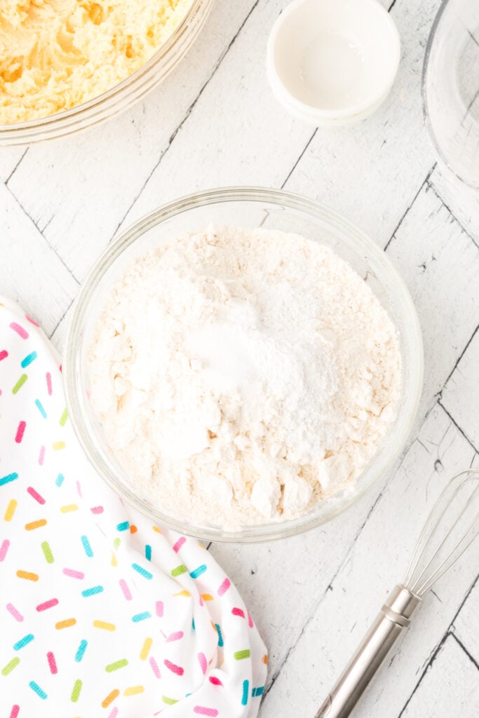 Dry ingredients including flour, baking powder, and salt combined in a bowl with a whisk beside it.