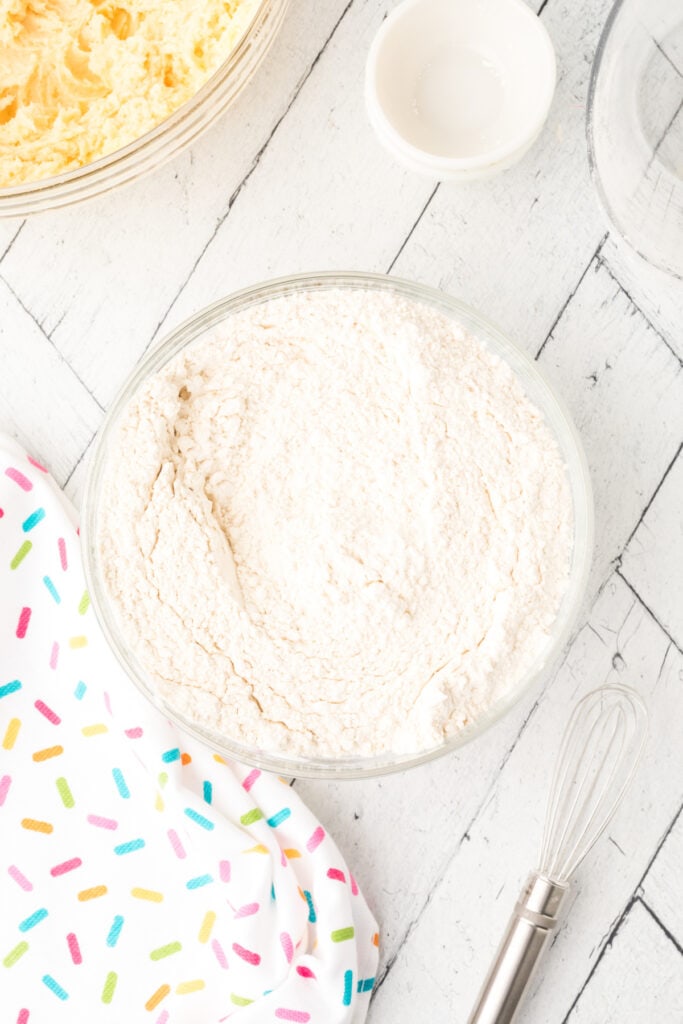 Bowl of dry ingredients whisked together for soft sugar cookies with cookie dough mixture visible at the side.