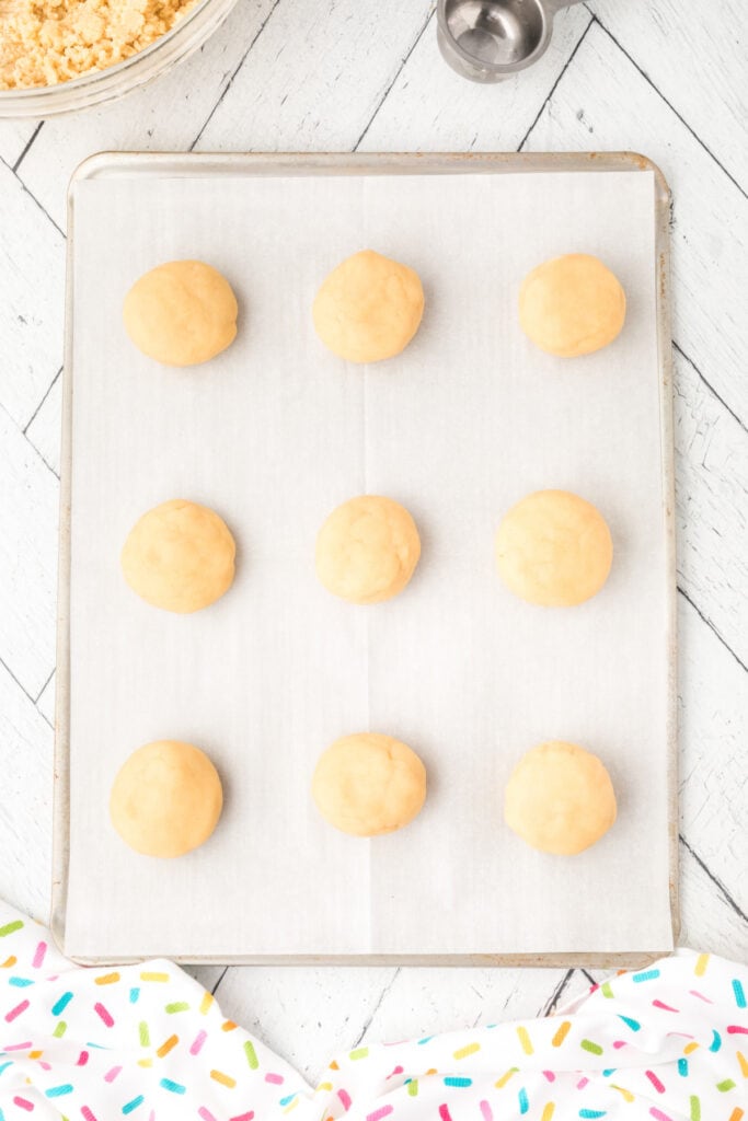 Balls of cookie dough evenly spaced on a parchment-lined baking sheet.