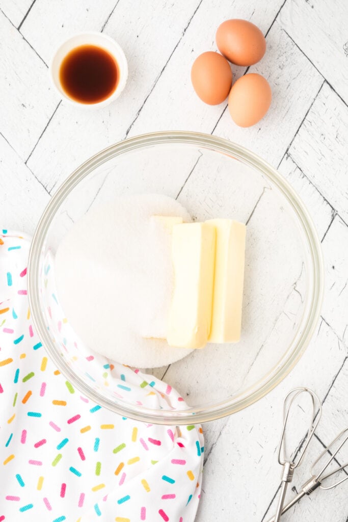 Butter and sugar in a mixing bowl with eggs and vanilla nearby, ready to begin creaming for soft sugar cookies.