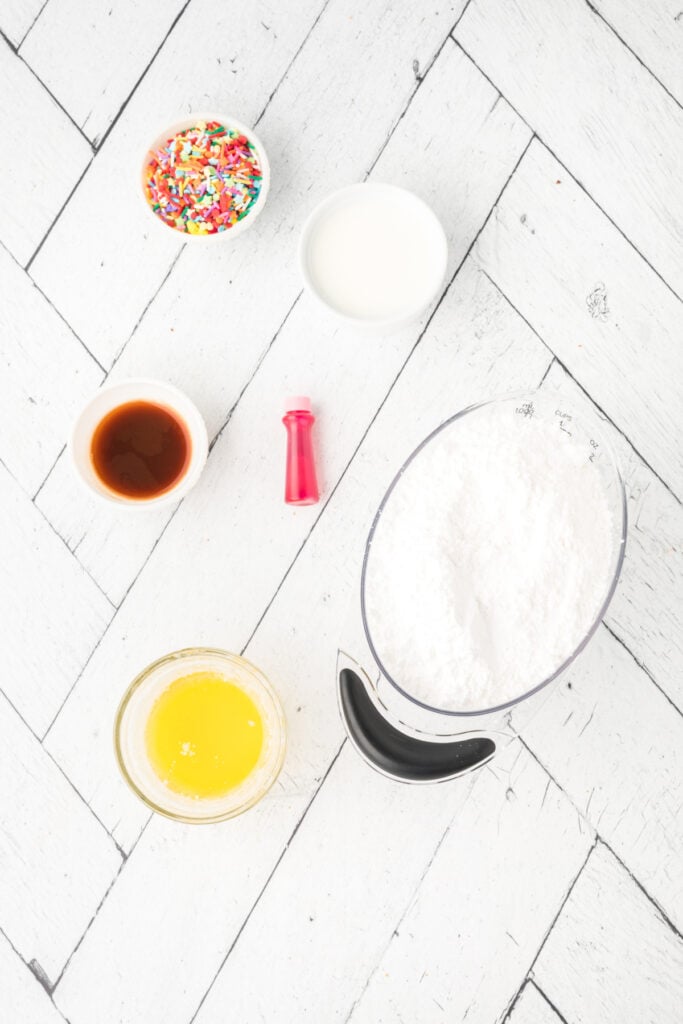 Frosting ingredients including powdered sugar, melted butter, milk, vanilla, food coloring, and sprinkles on a white background.