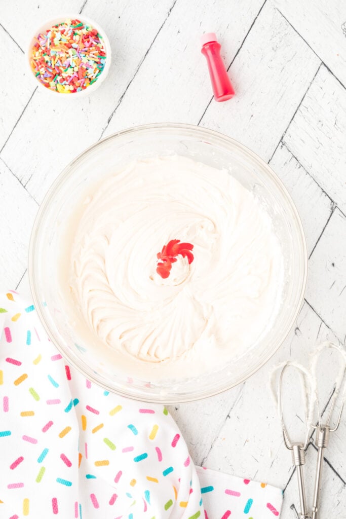 White frosting with drops of red food coloring added in the center of the bowl.