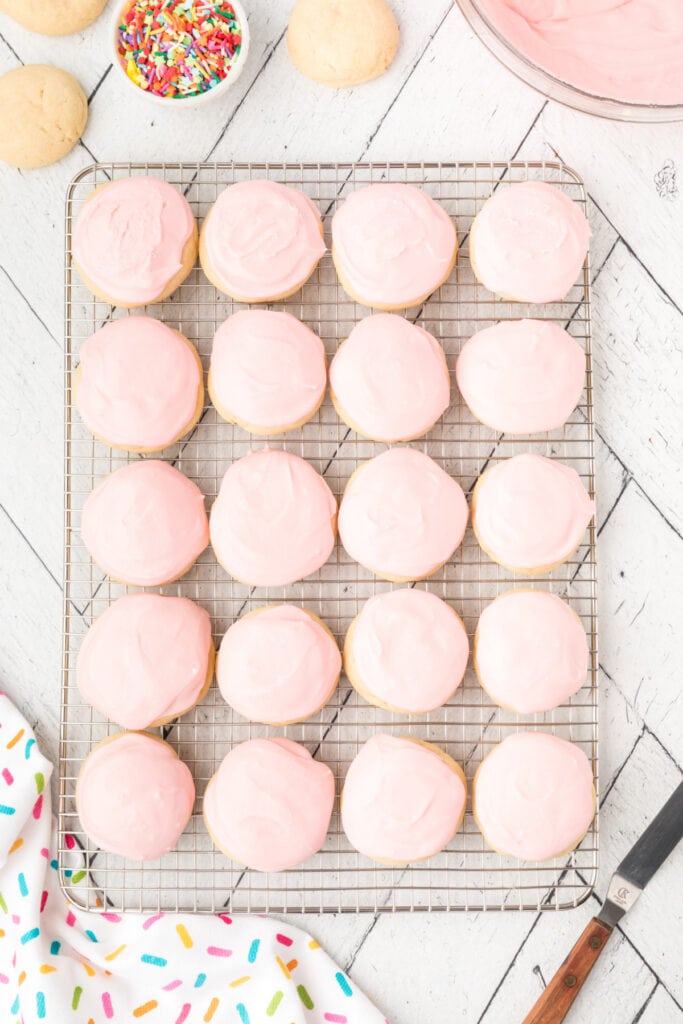 Freshly frosted soft sugar cookies with pink icing cooling on a wire rack.