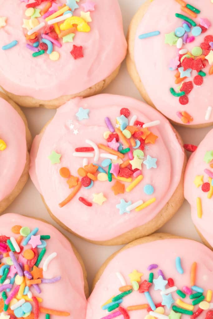Overhead close-up of frosted sugar cookies with colorful sprinkles, grouped together on a plate.